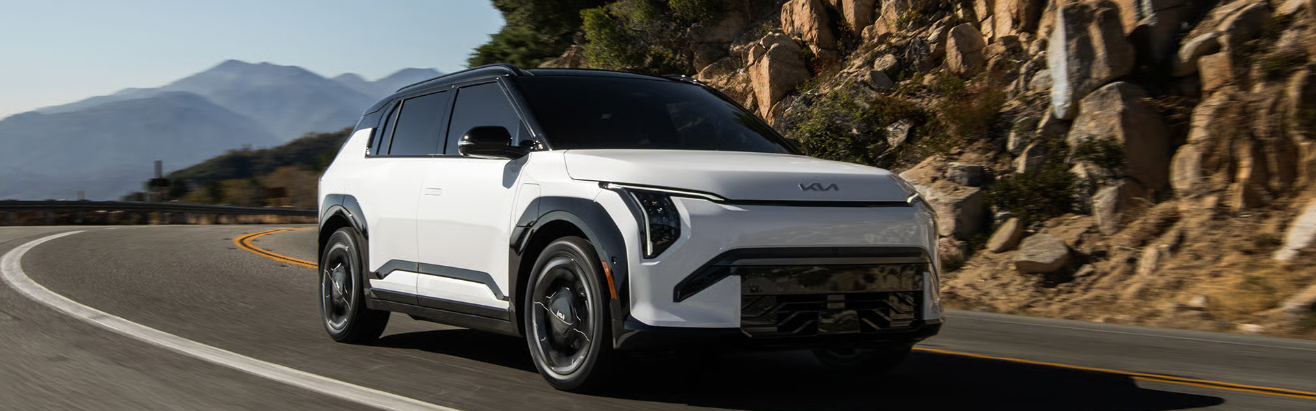 2027 Kia EV3 white electric SUV driving along a winding mountain road